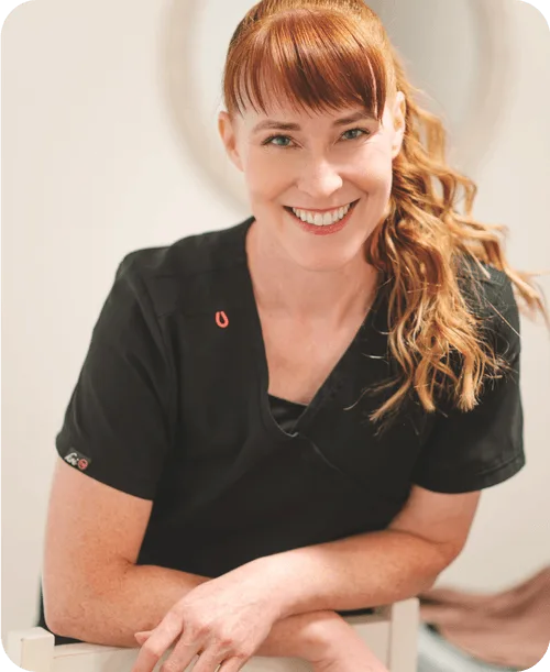 Female esthetician in black uniform with auburn hair with crossed hands.
